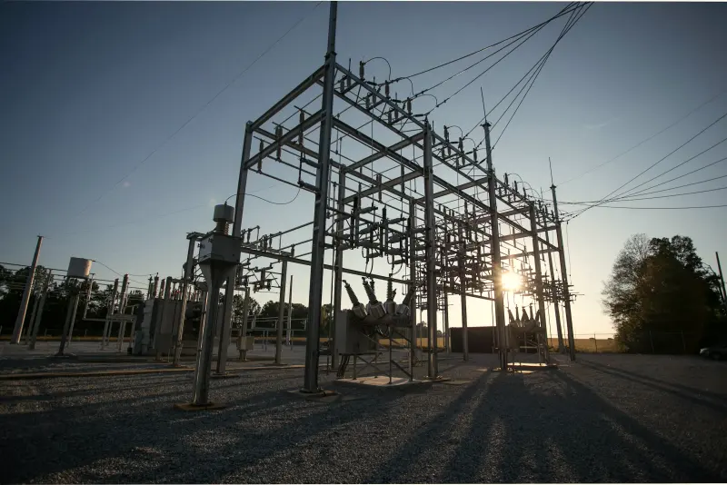 An electrical substation's steel gantries and transformers against a low evening sun.